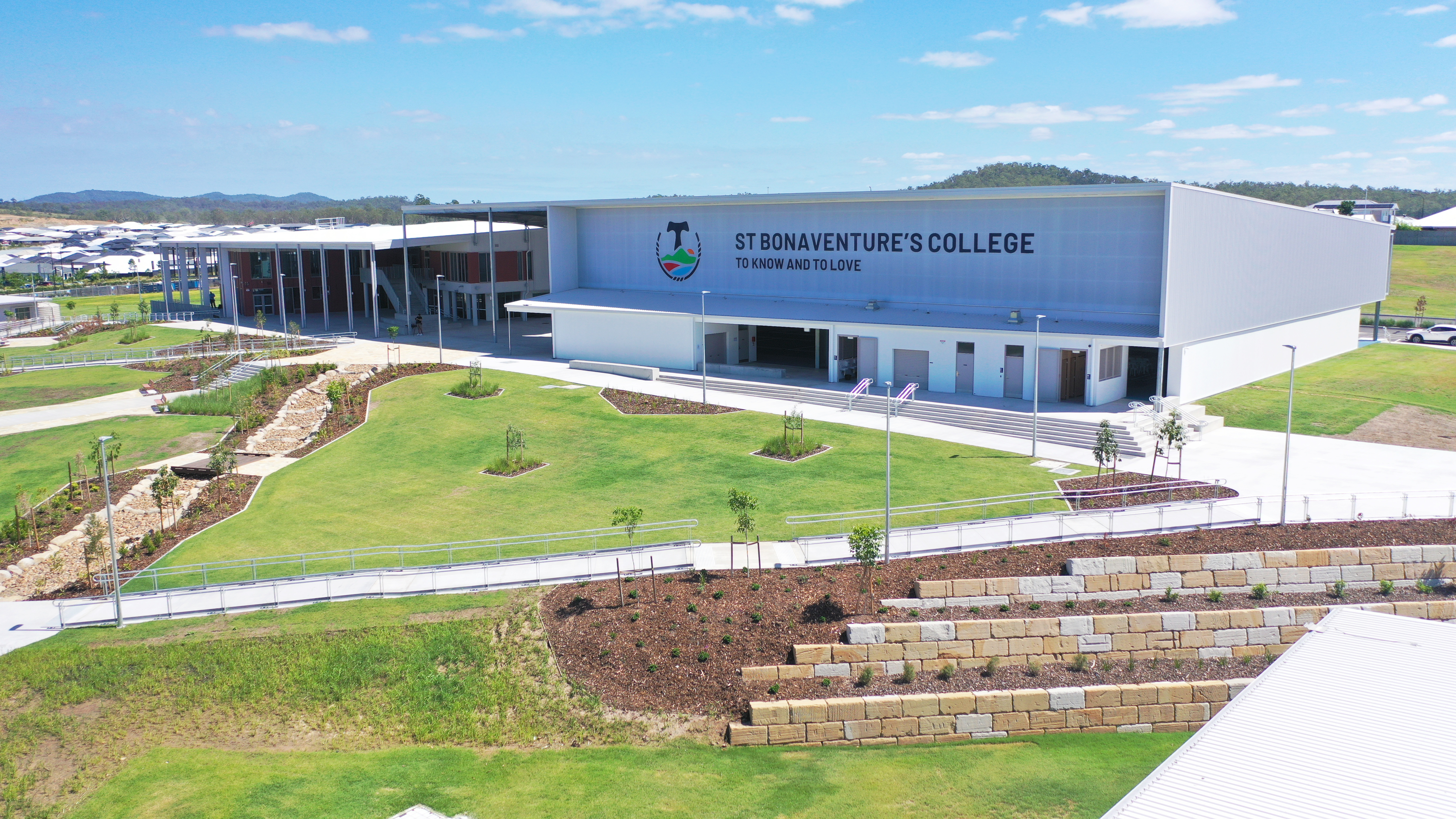 Aerial view of St Bonaventure’s College campus with modern buildings, landscaped grounds, pathways, and green open space under a blue sky